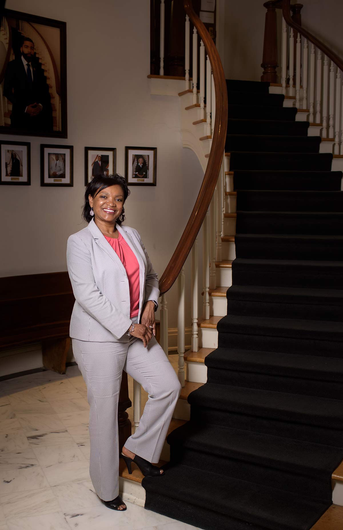 A smiling woman in business attire standing at the bottom of a staircase.