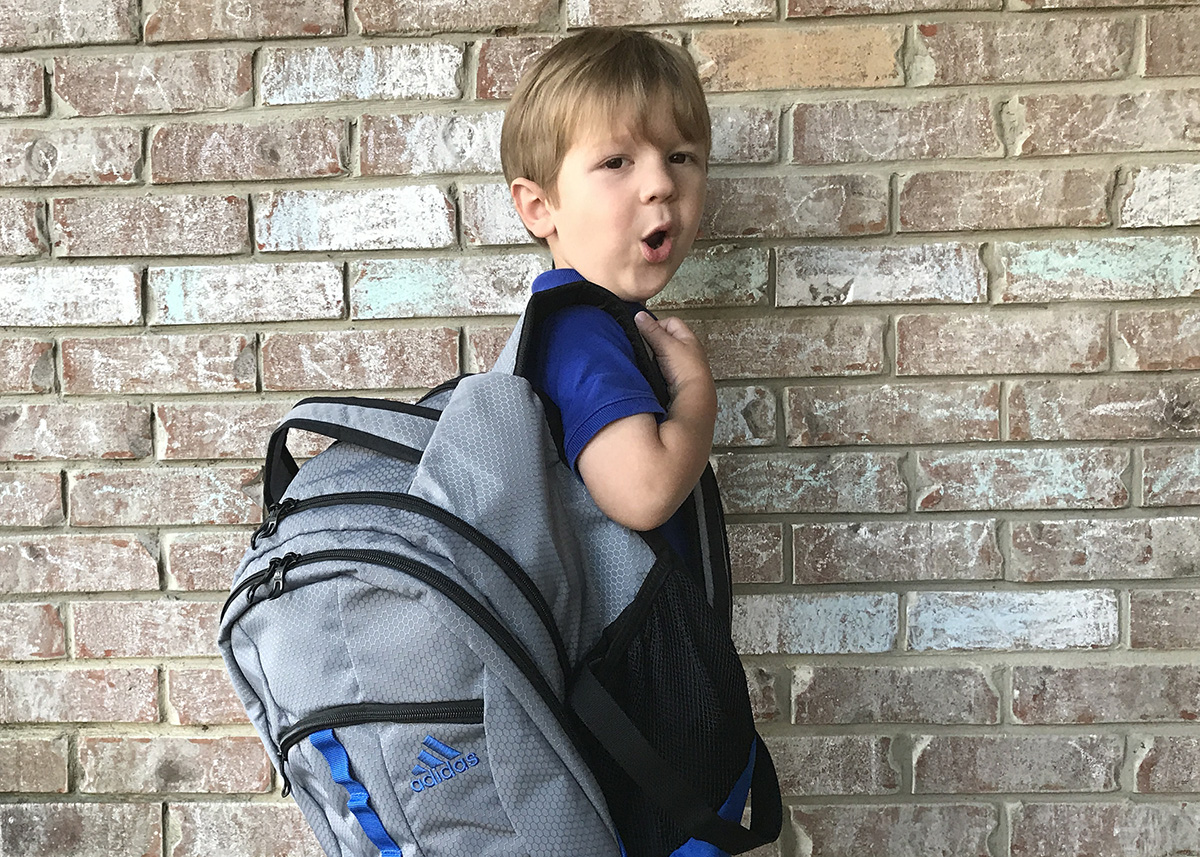 : Little boy wears backpack on one shoulder to demonstrate an incorrect way to carry it.