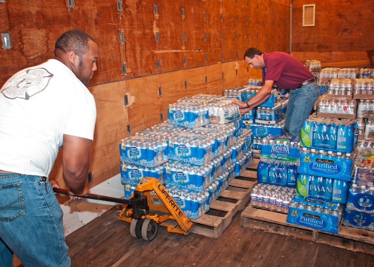 Two people moving pallets of bottled water.