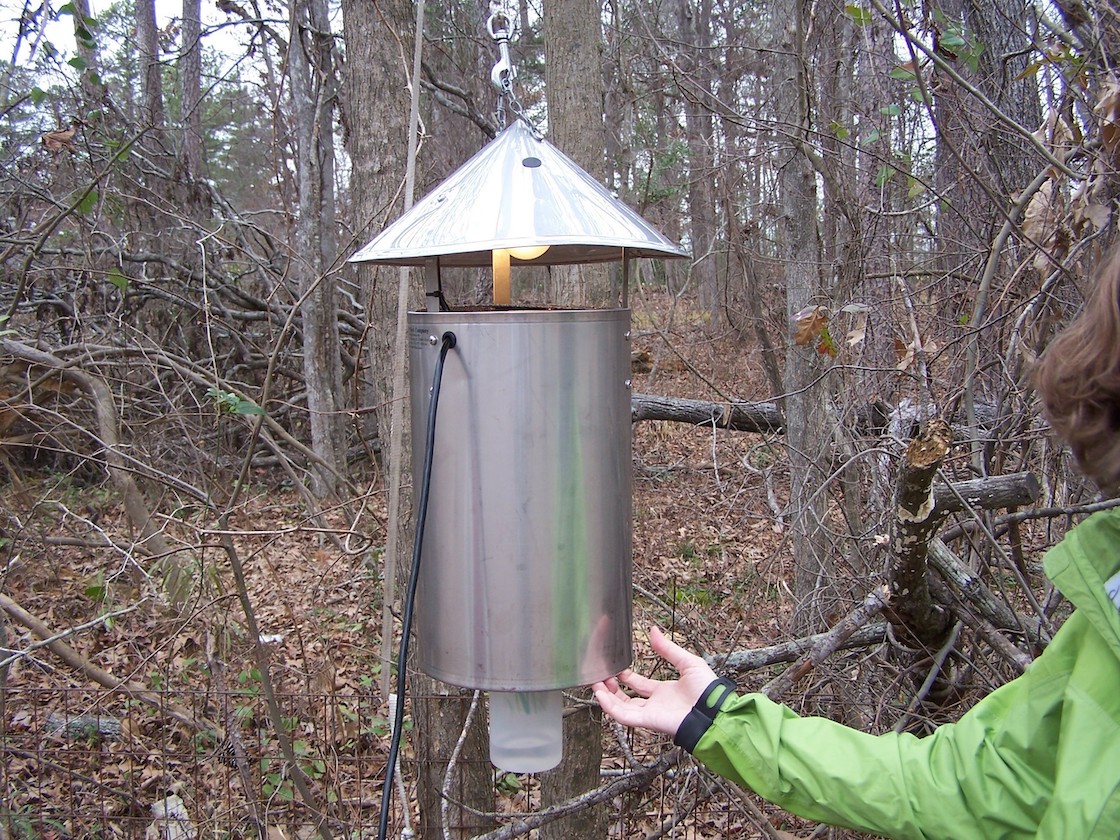A light with a metal cylinder hanging under it to trap mosquitoes.