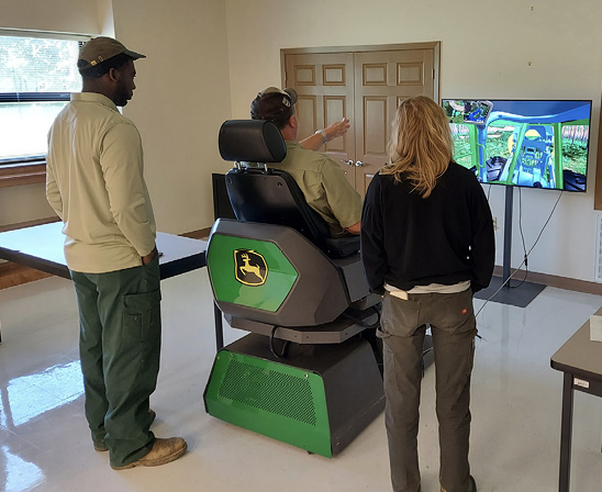 An instructor guides two trainees through a video simulation.