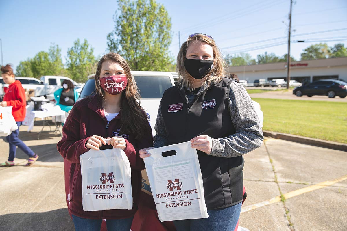 Two young women wearing Mississippi State University clothing hold while plastic bags with the MSU Extension Service logo.