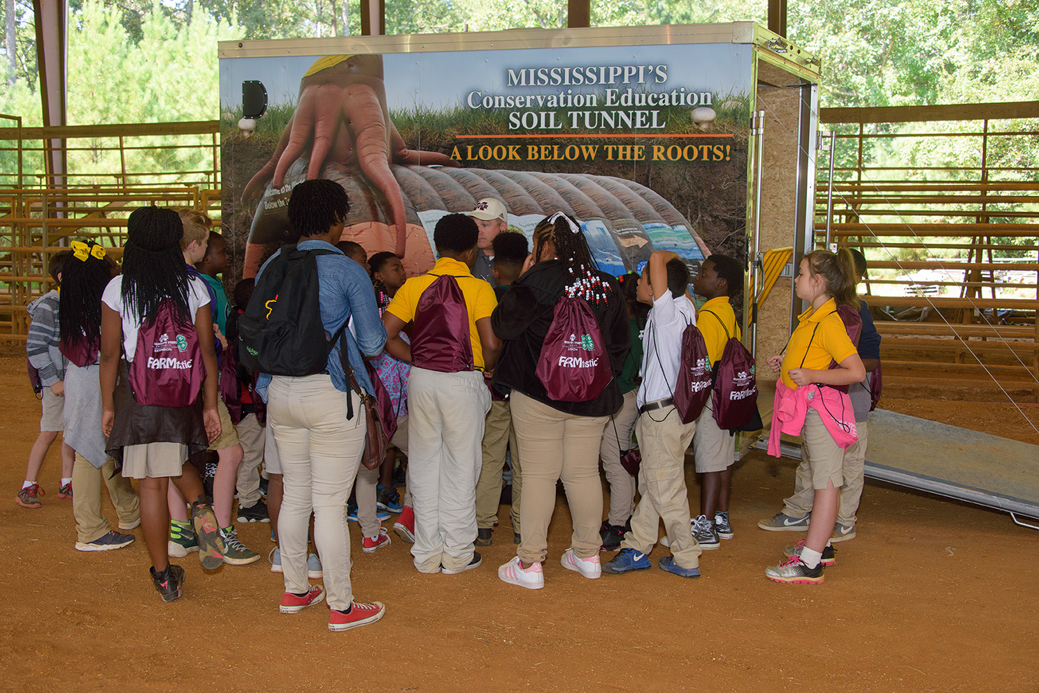 Elementary-age students wearing school uniforms gather around the soil tunnel truck to learn about the importance of soil before walking through the tunnel that gives them a look at what goes on underground.