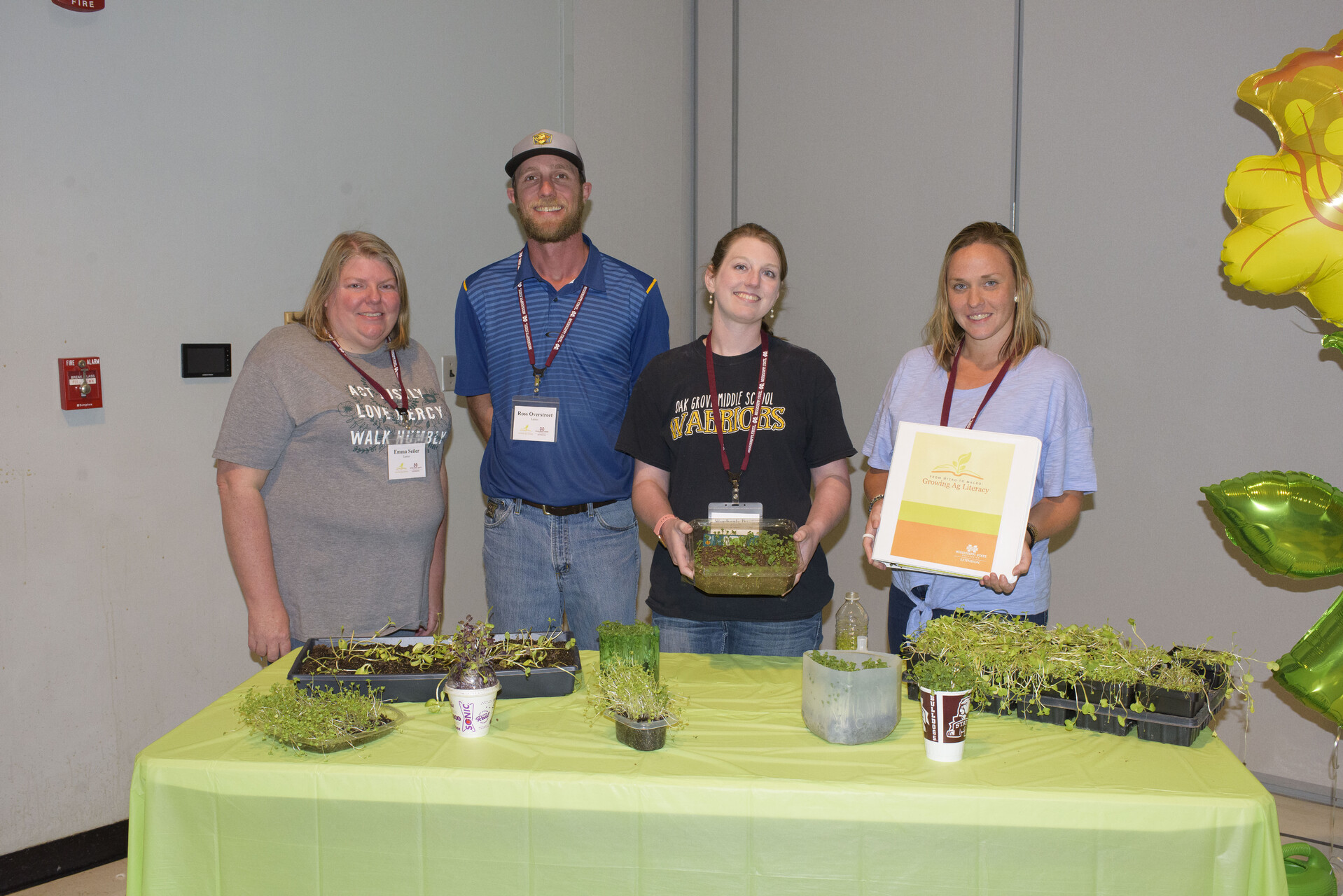 Three women and one man pose in front of a table filled with containers of microgreens