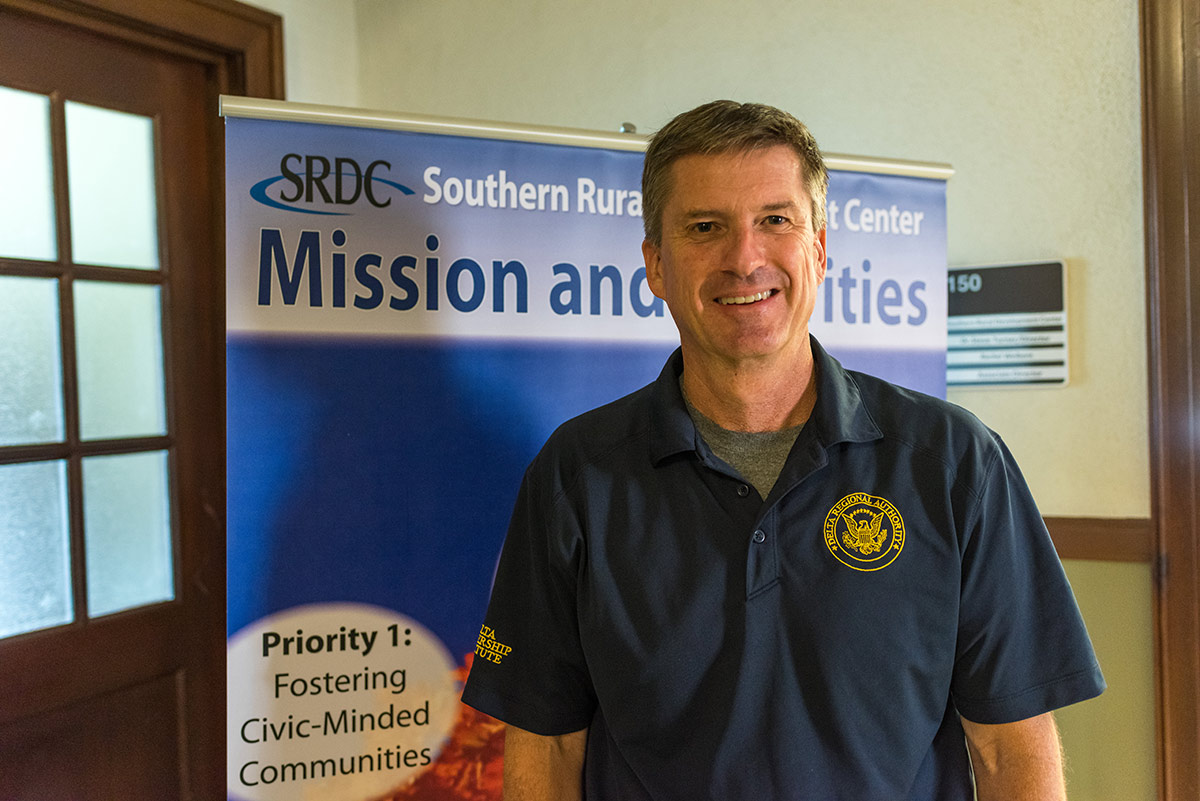 A smiling man stands in front of a sign advertising the Southern Rural Development Center