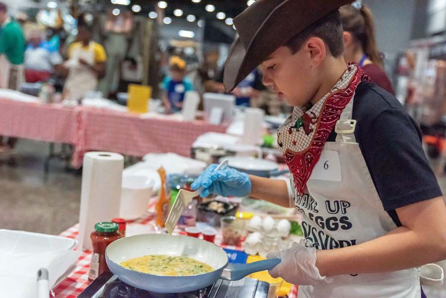 A boy wearing a cowboy hat and red scarf hold a spatula.
