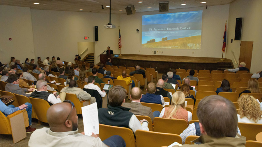People sitting in an auditorium with “U.S. Agricultural Economic Outlook” showing on the screen at the front of the room.