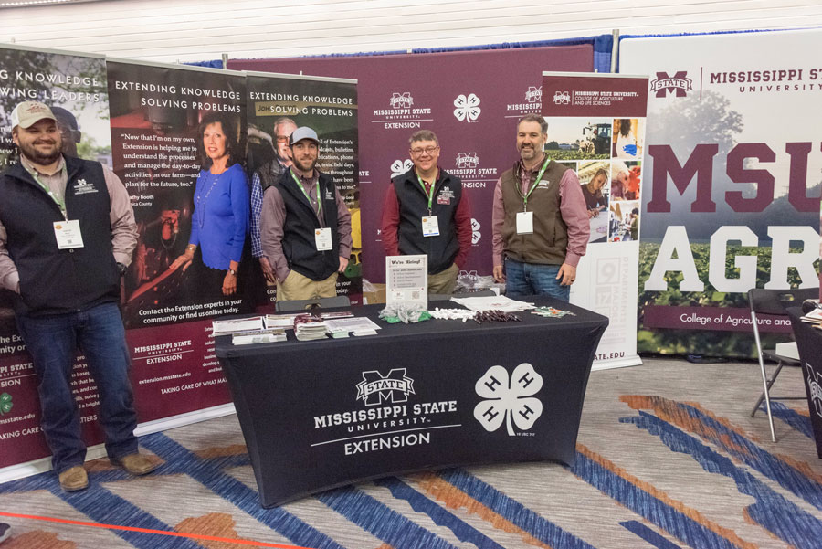 Four men stand at Mississippi State University Extension Service booth.