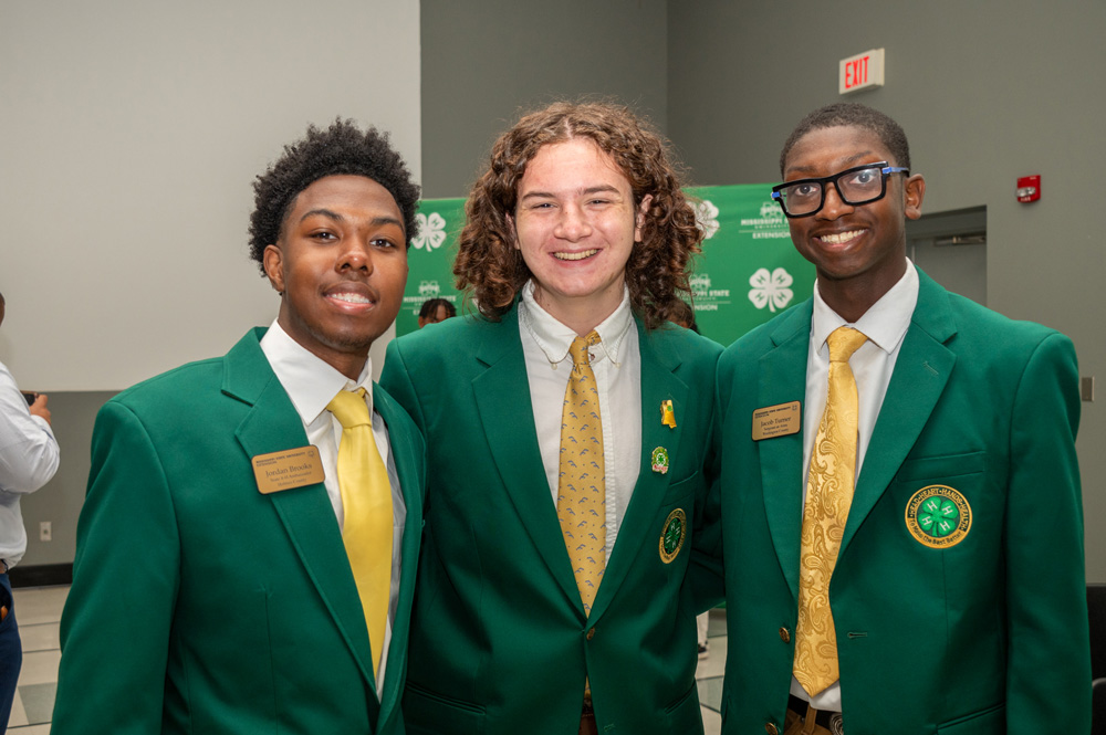 Three teens wearing green jackets and yellow ties, smiling.