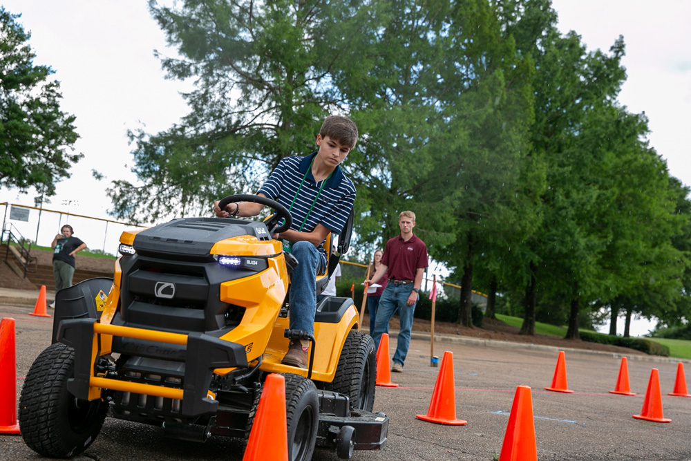 A teen driving a lawnmower through a course marked by safety cones.