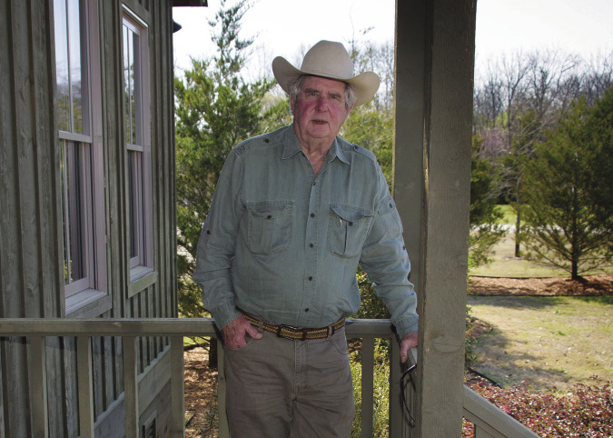 A man stands on a porch while leaning on the rail.