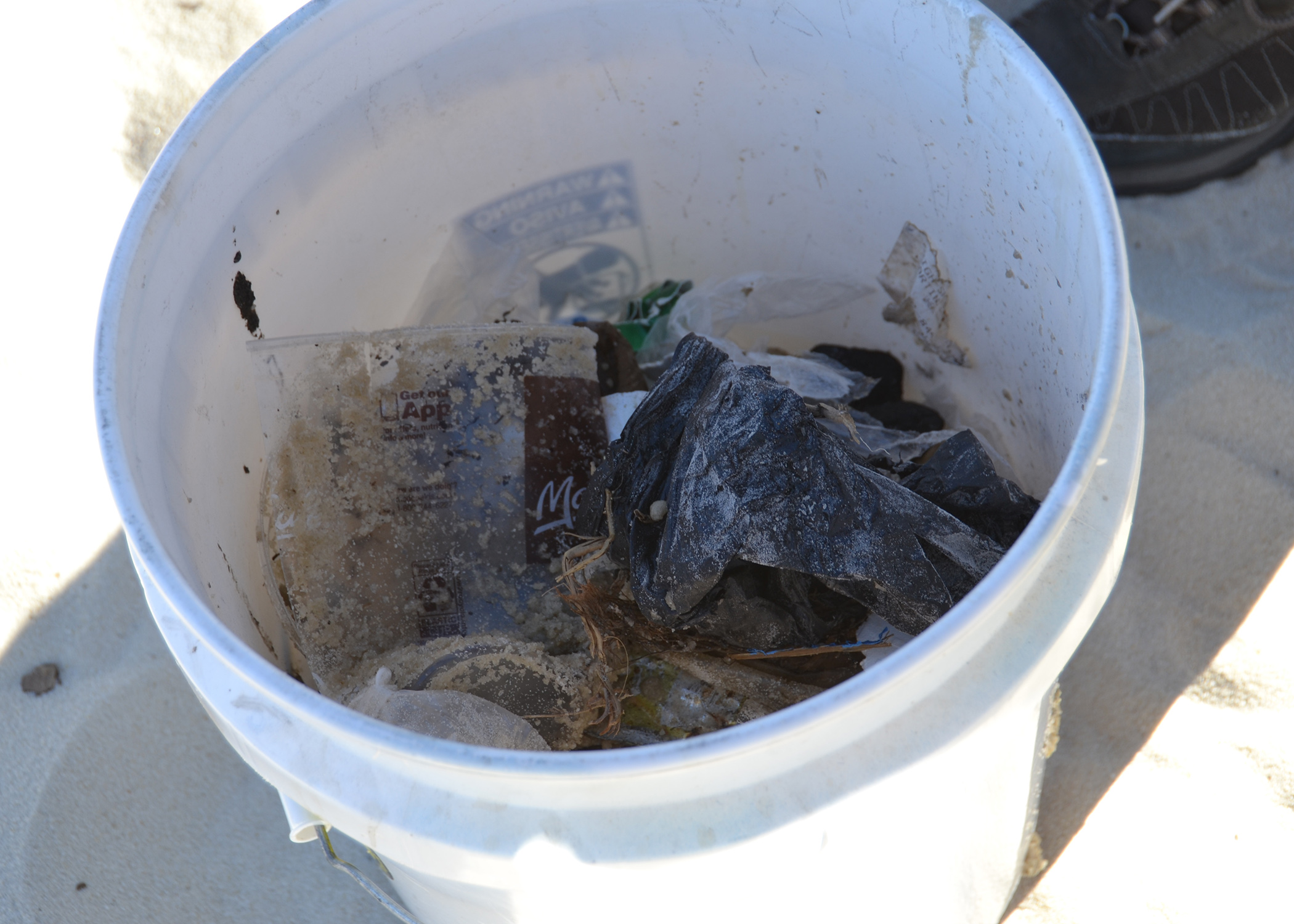 Trash, including plastic cups and plastic bags, fill a white five gallon bucket at a recent Mississippi Coastal Cleanup event in Biloxi, Mississippi.
