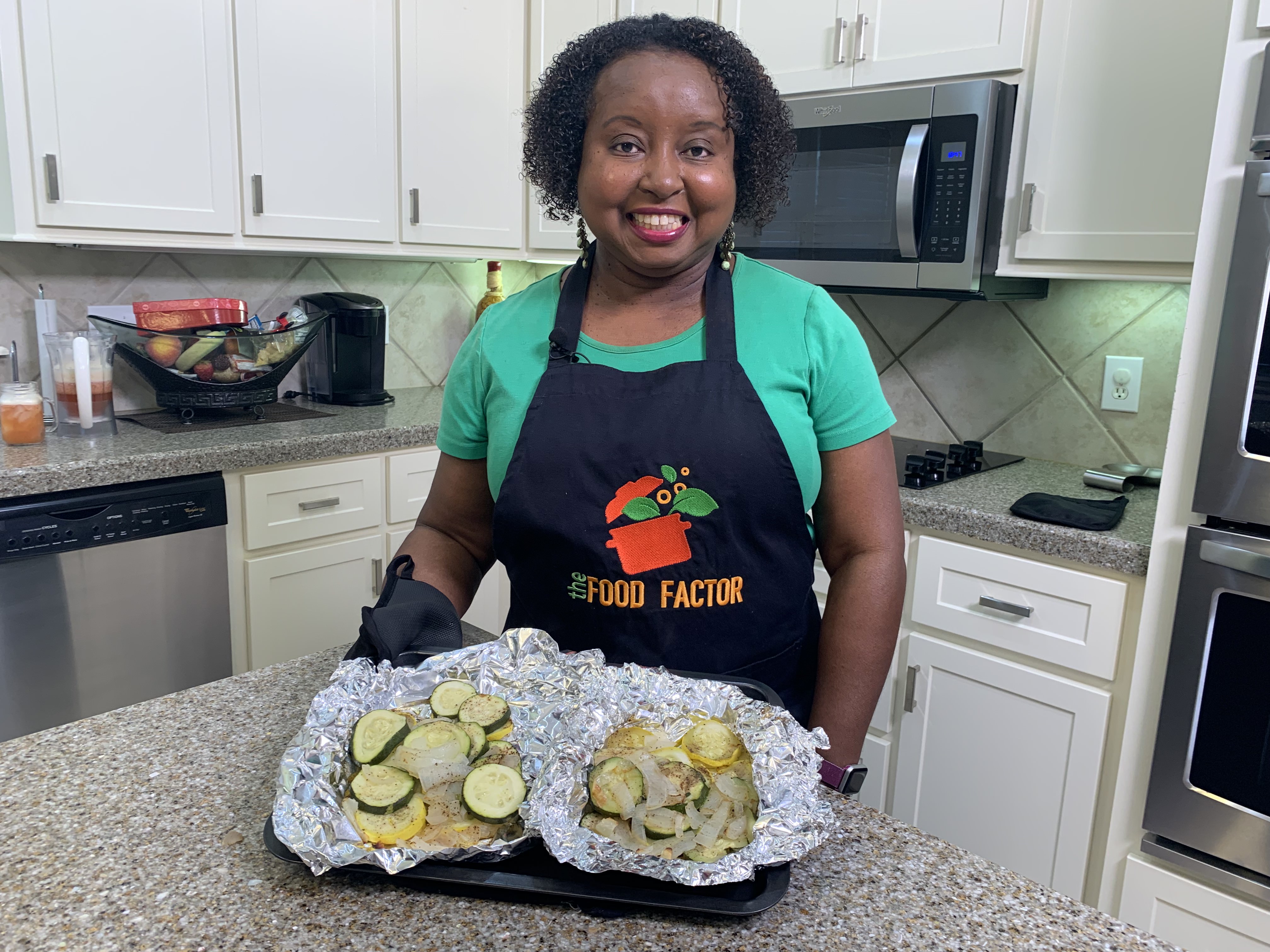 A woman stand in a kitchen with prepared food.