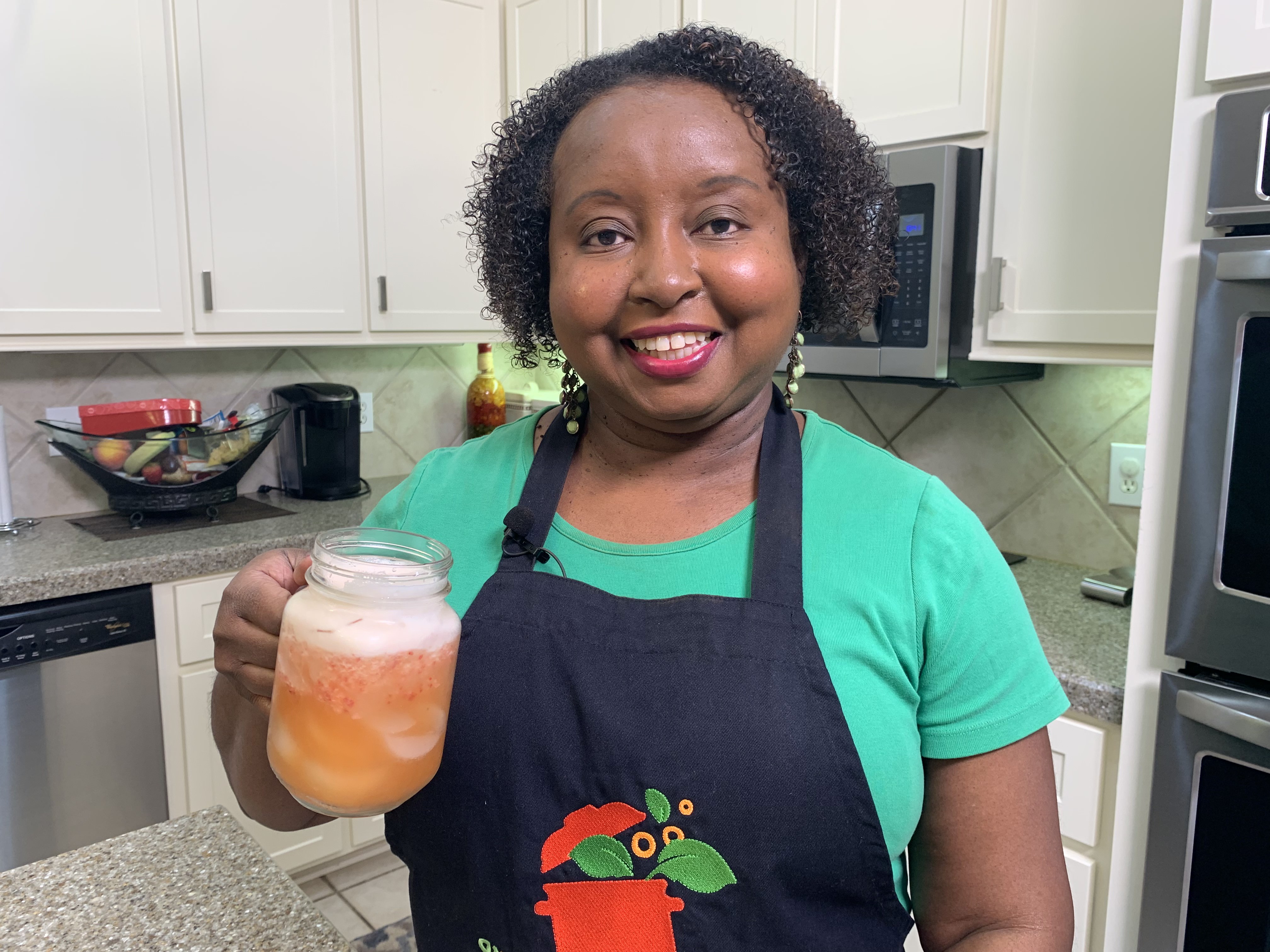 A woman in a kitchen holds a glass of strawberry pineapple lemonade.