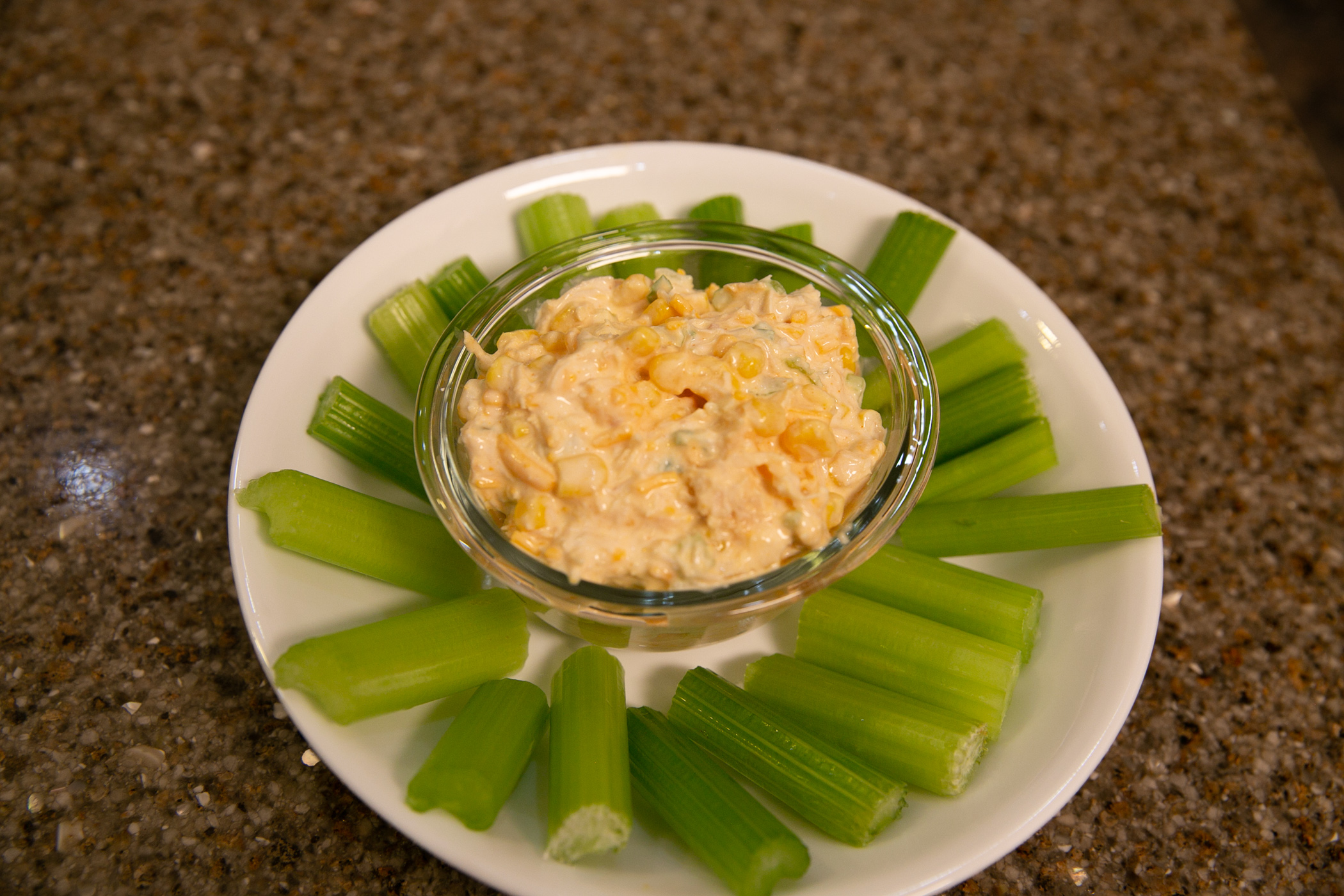 a bowl of Buffalo Chicken Dip stis on a plate surrounded by celery stalks