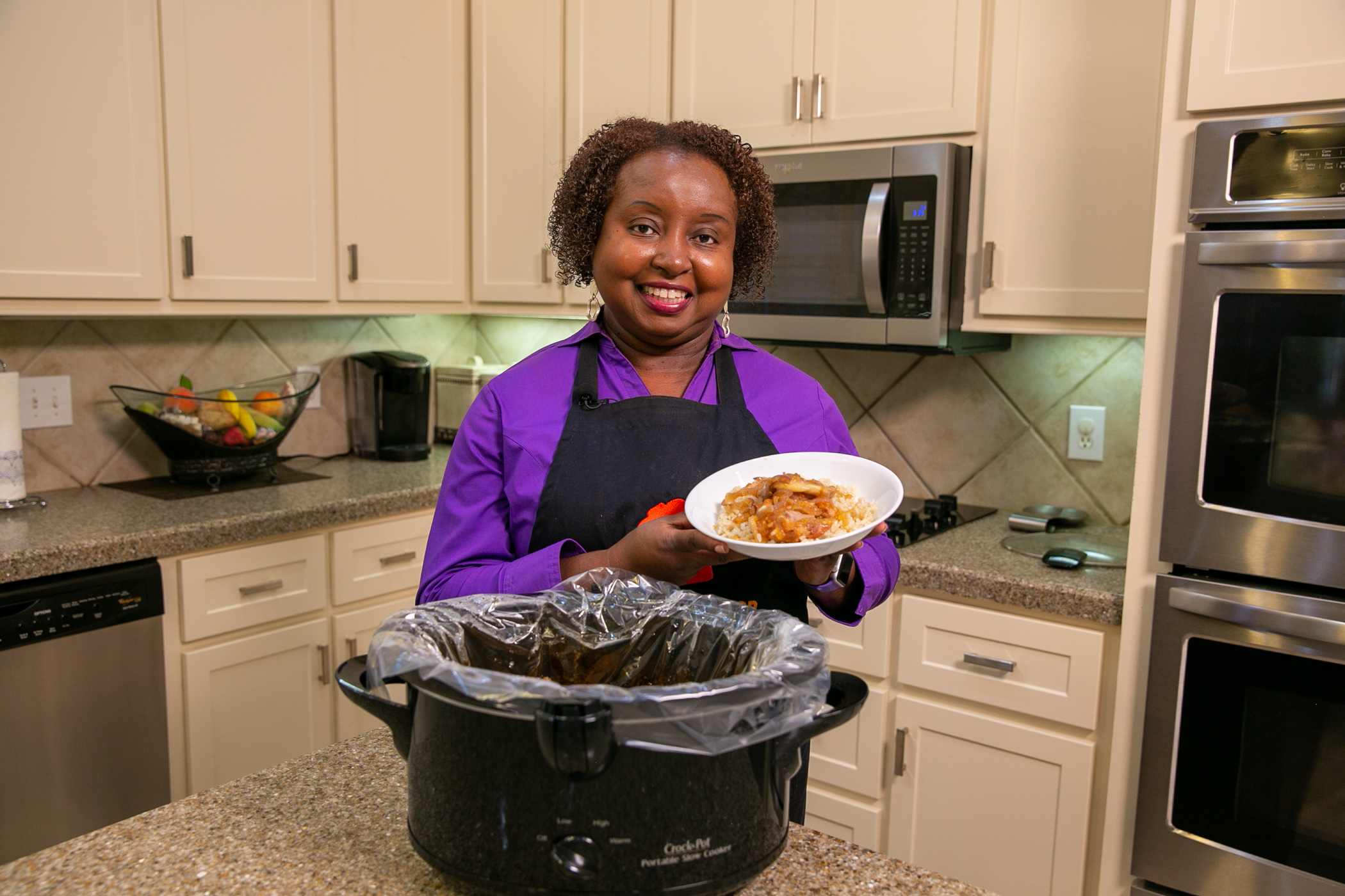 A woman stands in a kitchen and holds a serving of Chicken with Peachy Ginger Sauce.