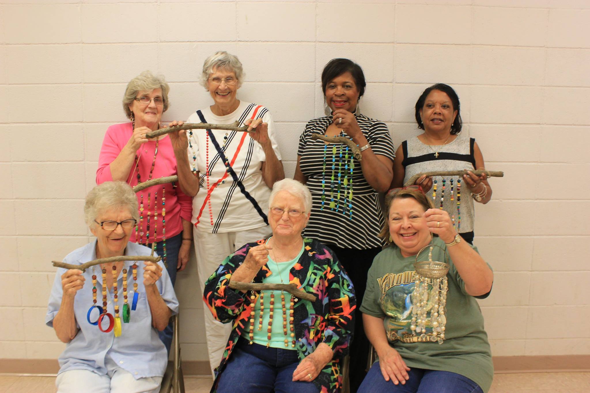 Seven women smile as they hold beaded windchimes.