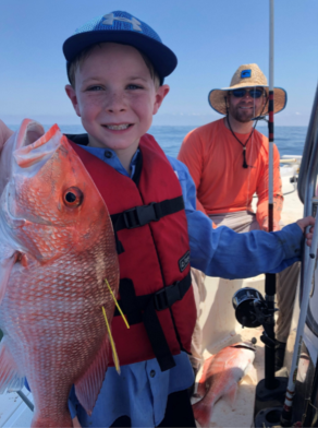 A young boy holding a red snapper.