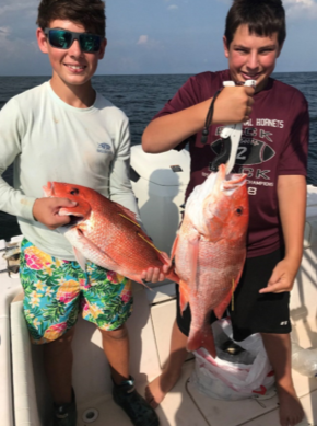 Two young boys each holding a red snapper.