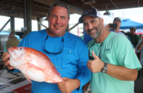 A man holding a red snapper while a man next to him gives a thumbs-up.