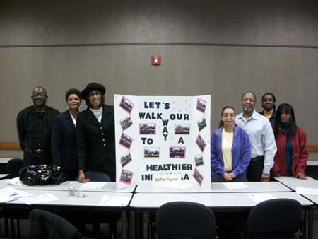 Seven people gather around a table and decorated presentation board saying, "Let's Walk Our Way To A Healthier America."