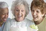 image of three female senior citizens laughing while looking at a birthday cake