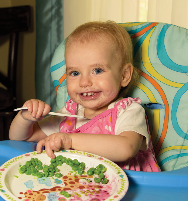 Smiling baby in high chair eating lunch.