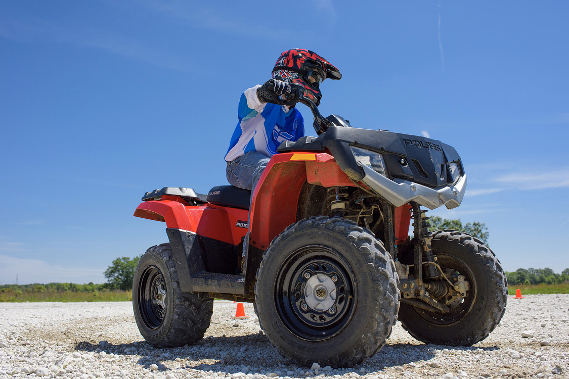 A young person wearing a helmet and protective gloves rides an ATV on a safety course.