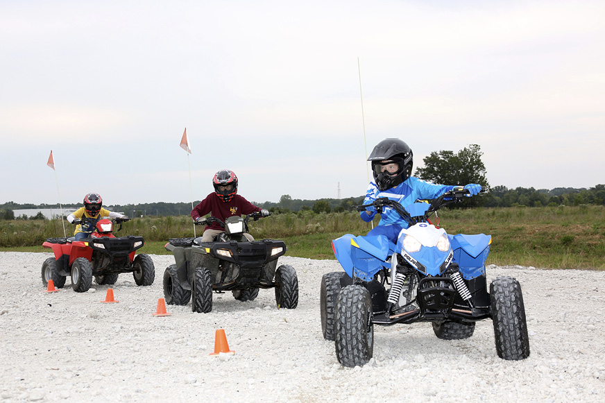 Three young people wearing helmets and other safety equipment ride ATVs on a safety course.