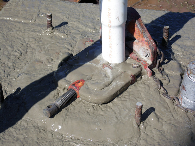 A well casing with a white pipe coming out of it, with a wet cement mixture around the base.