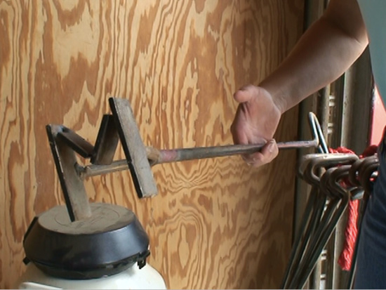 A person holds a hot branding iron in the shape of an M.
