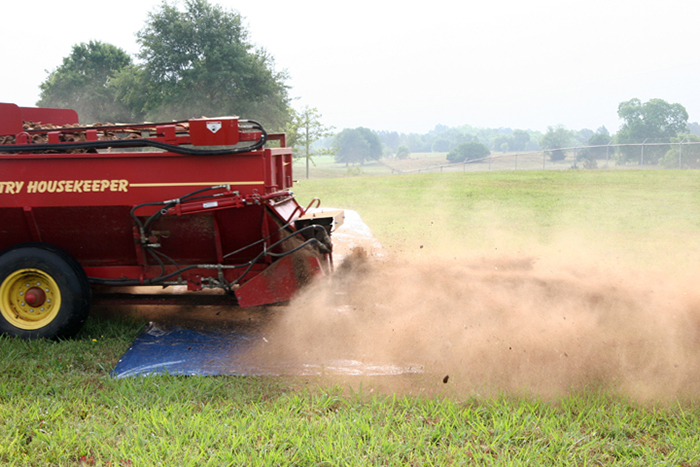 Image of a spreader spreading litter over a tarp, demonstrating the first part of step 4