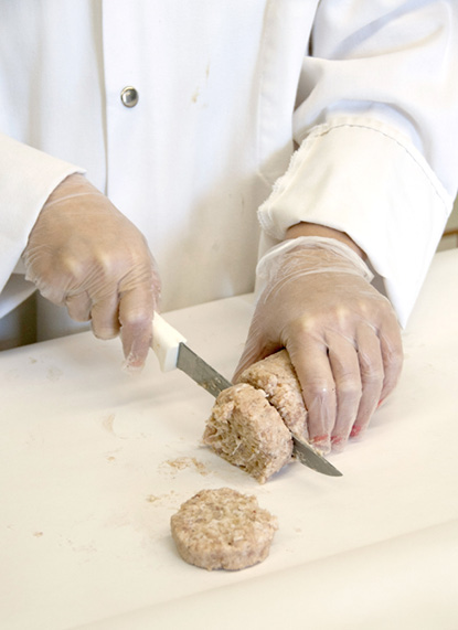 A person's gloved hands cut fresh sausage into patties.
