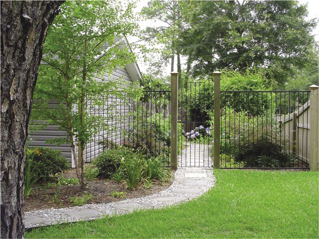 A walkway leading into a side yard garden behind a tall metal gate.
