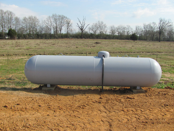 A propane tank anchored on the ground in front of a field.