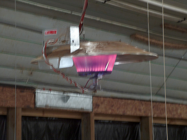 An infrared brooder hangs on wiring from the roof of a broiler house.