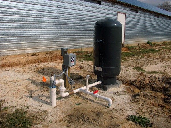 A well water pump in front of a metal-sided building.