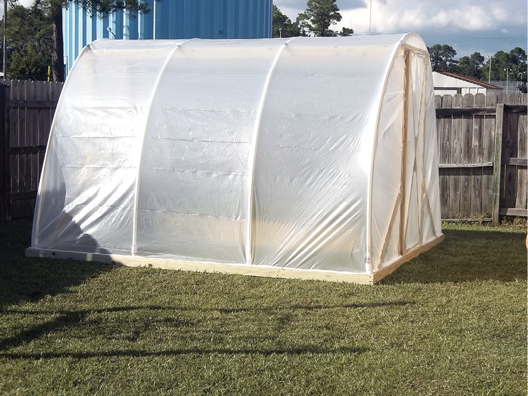 Wooden frame with arched roof covered in plastic sheeting.
