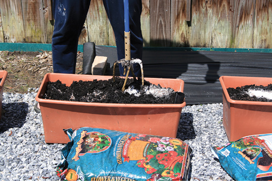 A person uses a garden claw to mix soil in a brown subirrigated container.