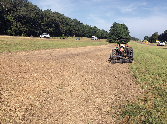 A tractor rides along a median to cultipack the seed into the soil surface. 