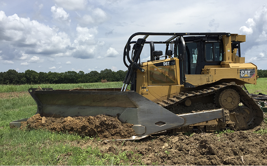 A bulldozer with a large attachment removes stems in a field.