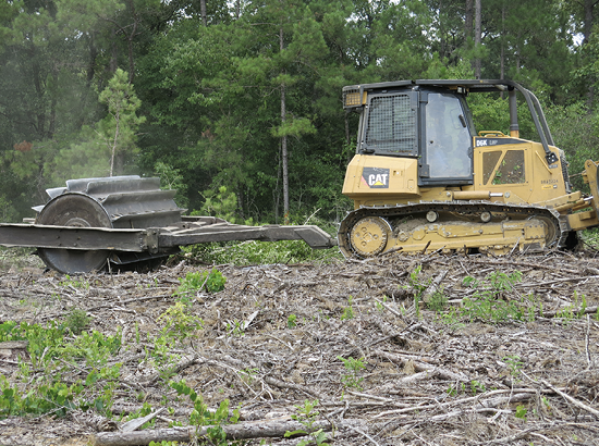 A bulldozer pulls a large, round implement over logging debris.