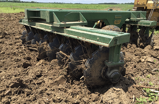 A disker is pulled over rough dirt ground.