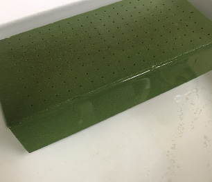 A green, rectangular block with tiny holes all over submerged in water.