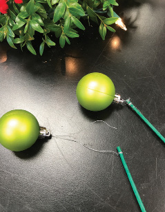 Two small, green ball ornaments attached with wire to green wooden picks.