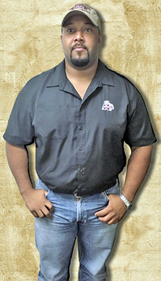 A man dressed in a button up shirt, blue jeans and cap.