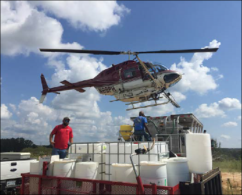 A helicopter is shown descending to the ground to refill with herbicide treatment for later use.