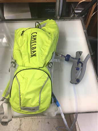 A neon green camelbak backpack that holds a pouch of fluid. There are hoses coming out of the backpack that allow the fluid to be drank or released. 