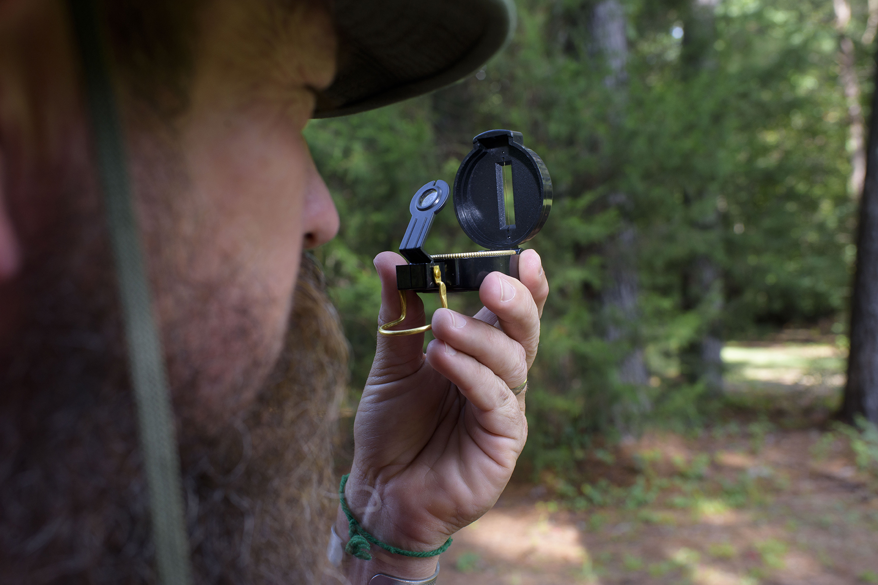A person holds a compass up and peers through it at an object in the distance.