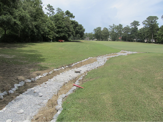 Ditch on a green golf course filled with gravel and lined with rocks.